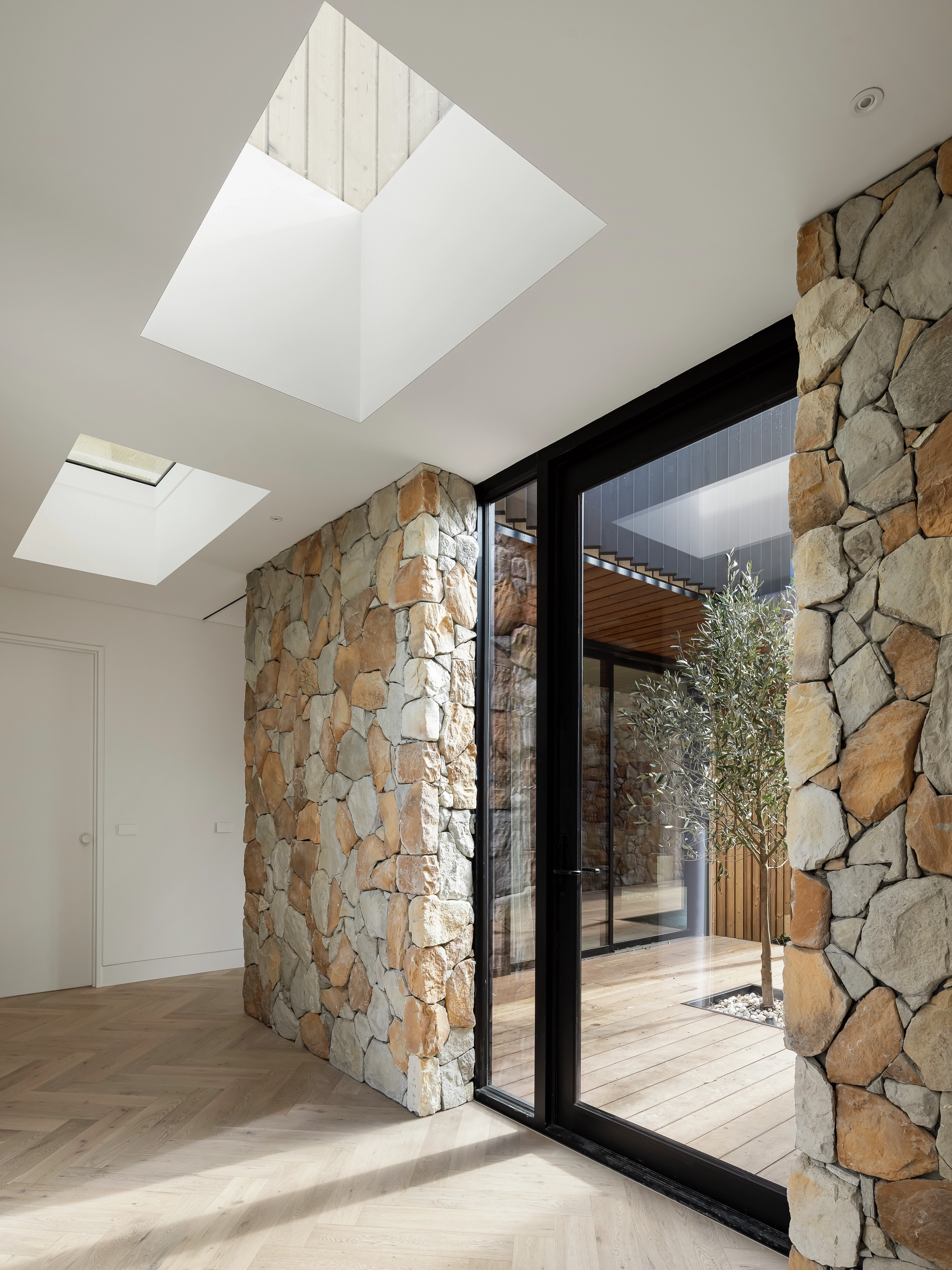 Modern stone-walled hallway lit by VELUX flat roof windows and glass doors to a small courtyard.