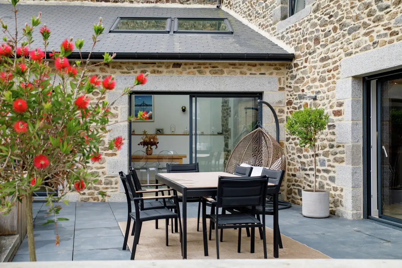 Terrasse fleurie et vue extérieure d’une véranda mansardée avec baie vitrée et duo de fenêtres de toit