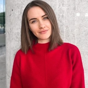 Young woman in a bright red sweater standing by a grey stone wall, smiling softly.