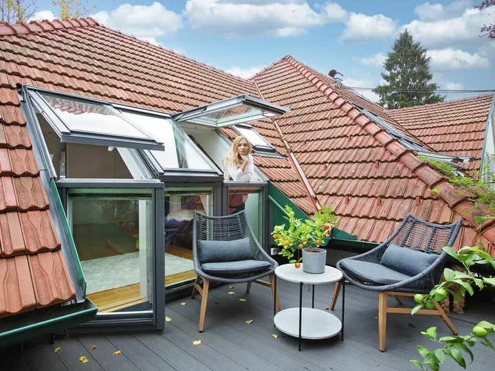 Moderne Dachterrasse mit VELUX Dachflächenfenstern, Korbstühlen und grünen Pflanzen.