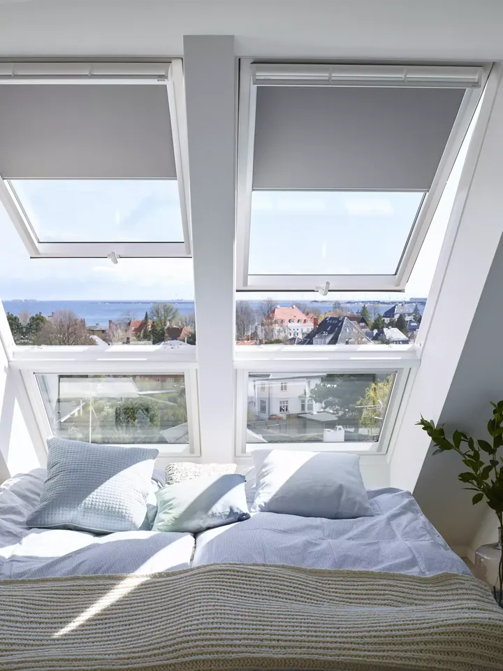 Gemütliches Dachboden-Schlafzimmer mit VELUX Dachflächenfenstern, die eine Aussicht auf den Himmel und das Stadtbild bieten.