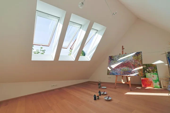 Helles Künstleratelier auf dem Dachboden mit VELUX Dachflächenfenstern und bunten Gemälden.
