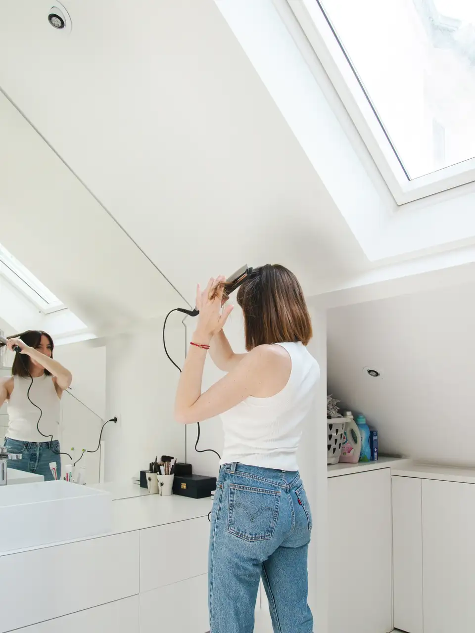 Une femme se prépare devant le miroir dans une salle de bain sous les combles éclairée par une fenêtre de toit VELUX