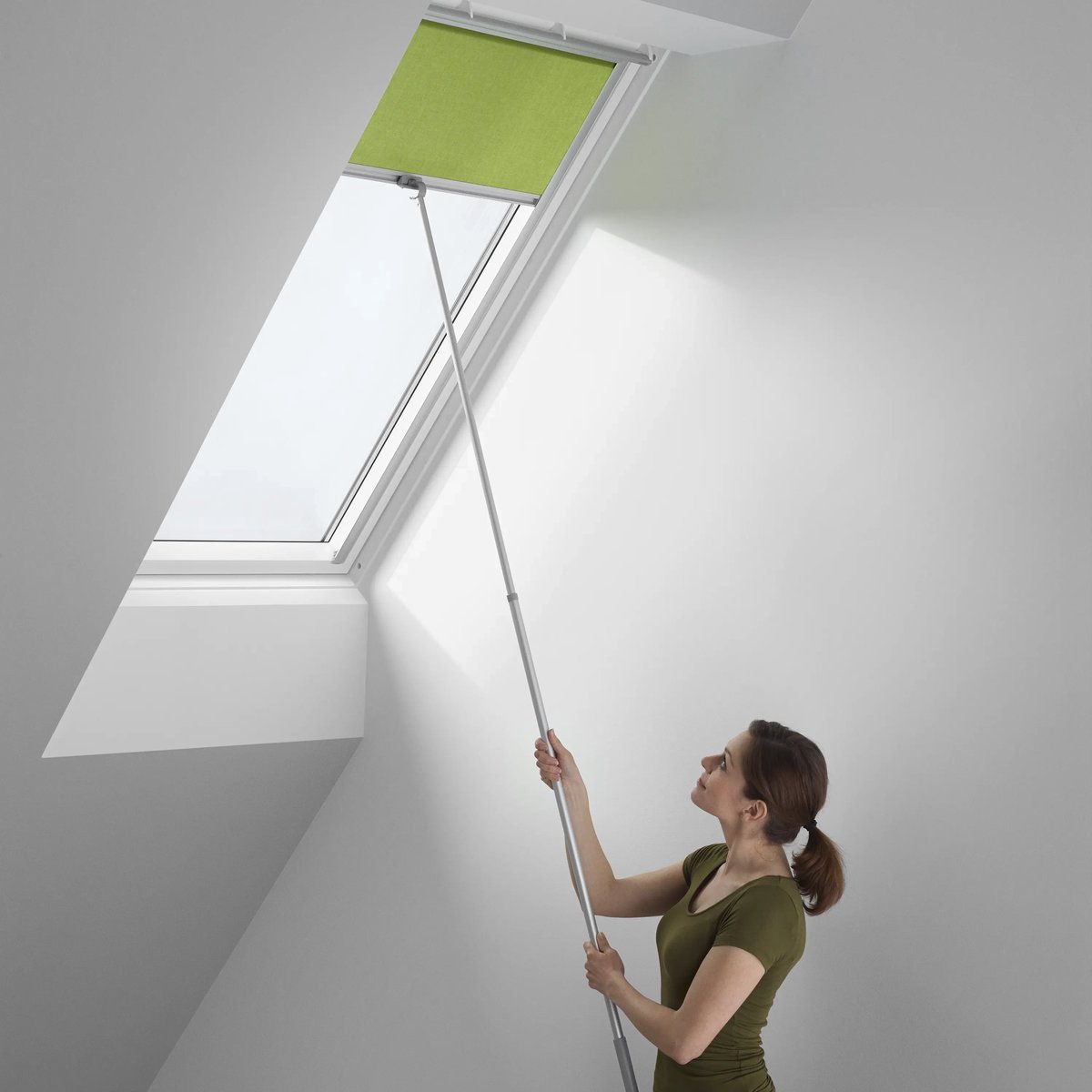 Person adjusting blind on VELUX roof window with a pole.