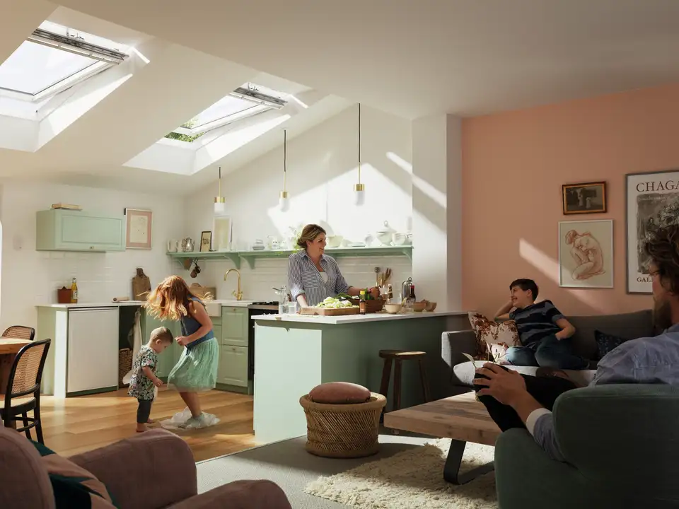 Una famiglia in un ampio open space con grande cucina e due finestre per tetti VELUX aperte per ventilare.