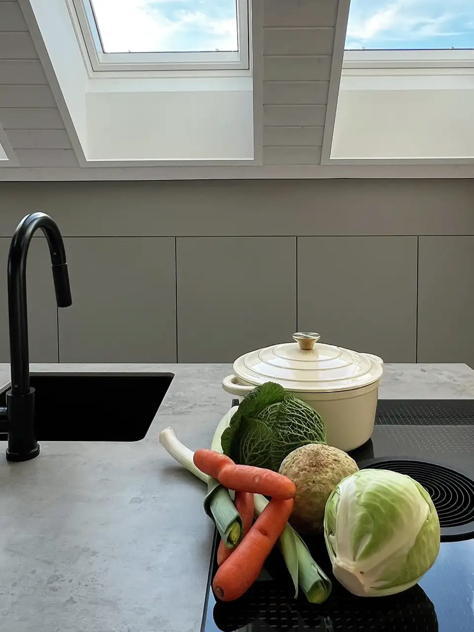 Moderne keuken met zwarte kraan, wit werkblad en groenten onder VELUX dakramen.