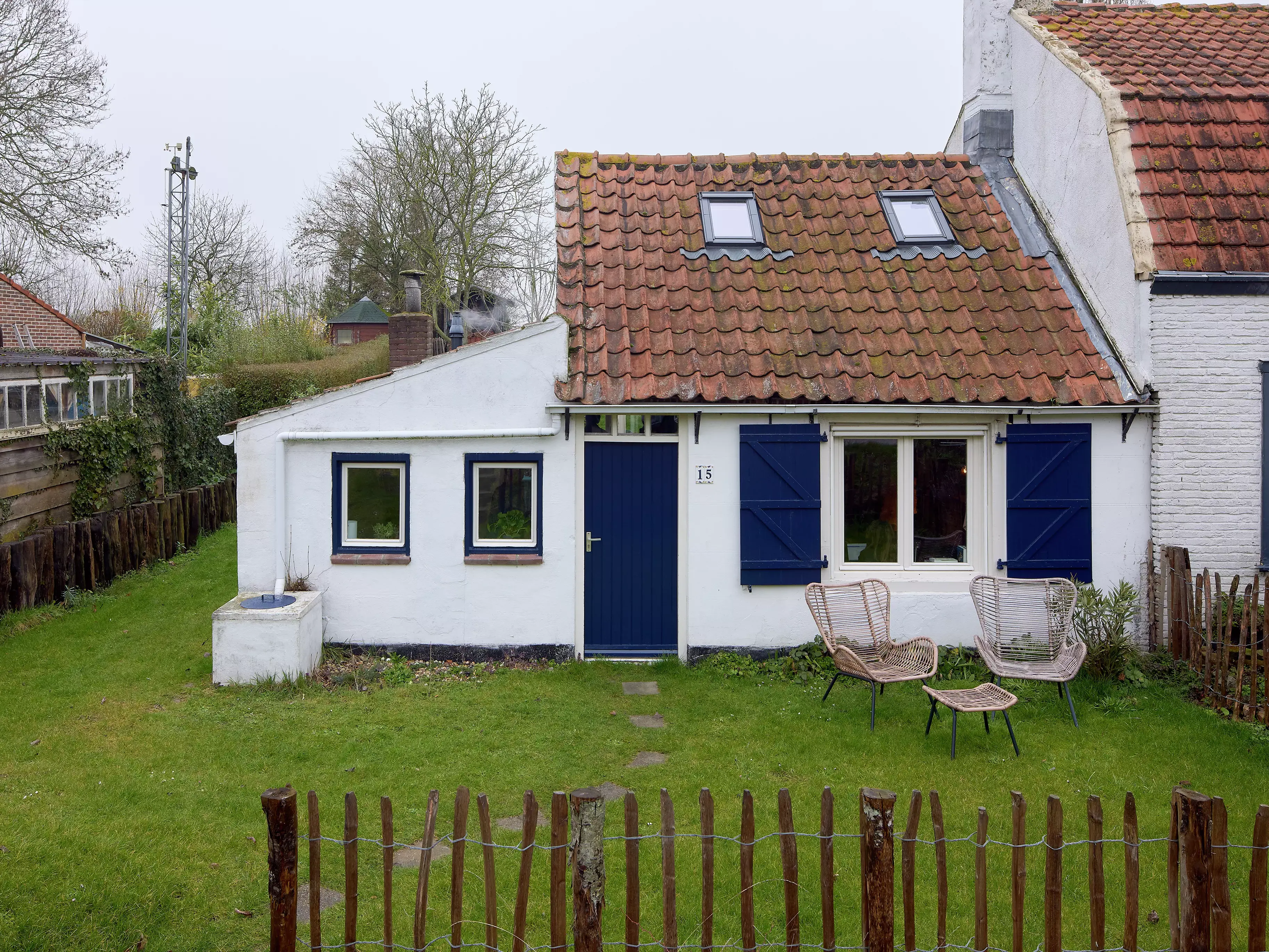 Cottage jumelé avec des murs blancs, des volets bleus et des fenêtres de toit VELUX.