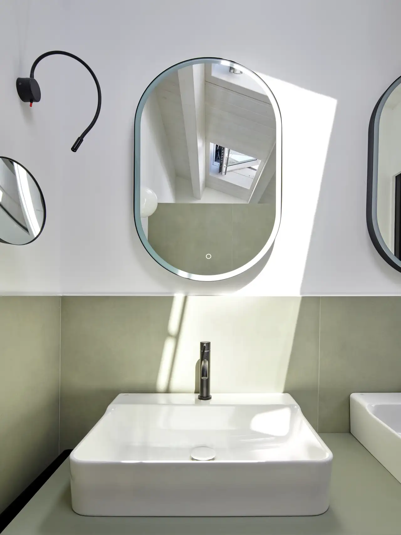 Specchio moderno con cornice sottile che riflette la luce naturale in ingresso da una finestra per tetti