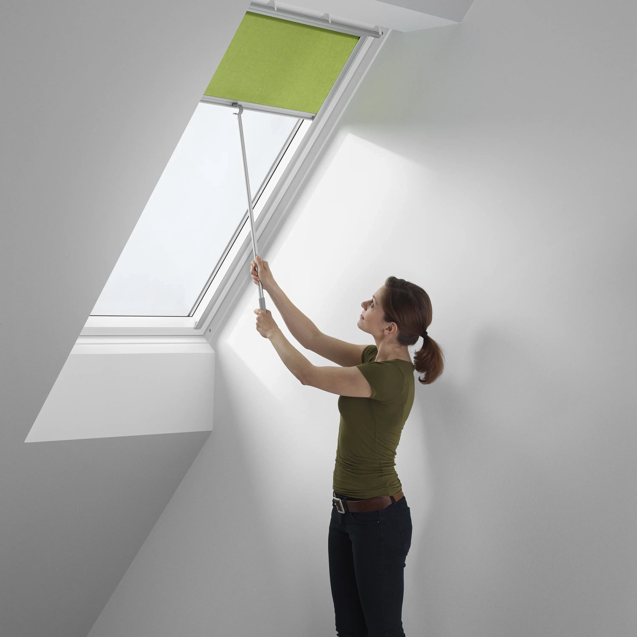 Person adjusting blind on VELUX roof window in attic room.