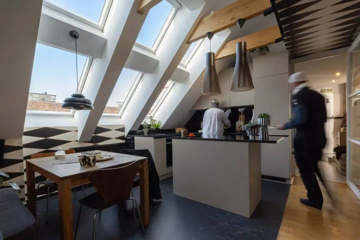 Moderne Küche mit VELUX Dachflächenfenster, geometrischem Wanddesign und einer Person beim Kochen.