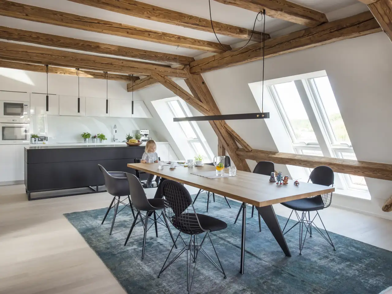 Moderne, offene Küche im Wohnesszimmer mit Dachschräge und hölzernen Dachbalken| VELUX Magazin
