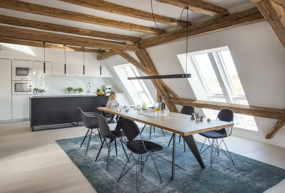 Cucina e zona pranzo in mansarda con finestre per tetti VELUX e luci dal design minimalista sul piano della cucina e sul tavolo.