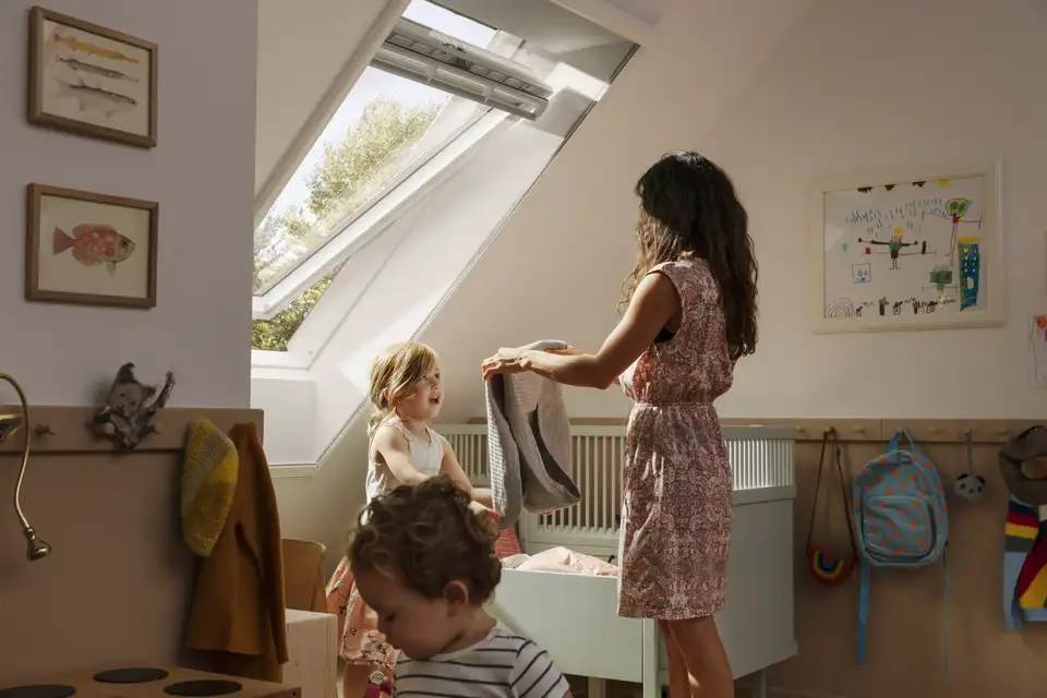 Une femme et une fillette dans une chambre près d’une fenêtre de toit protégée par une moustiquaire.