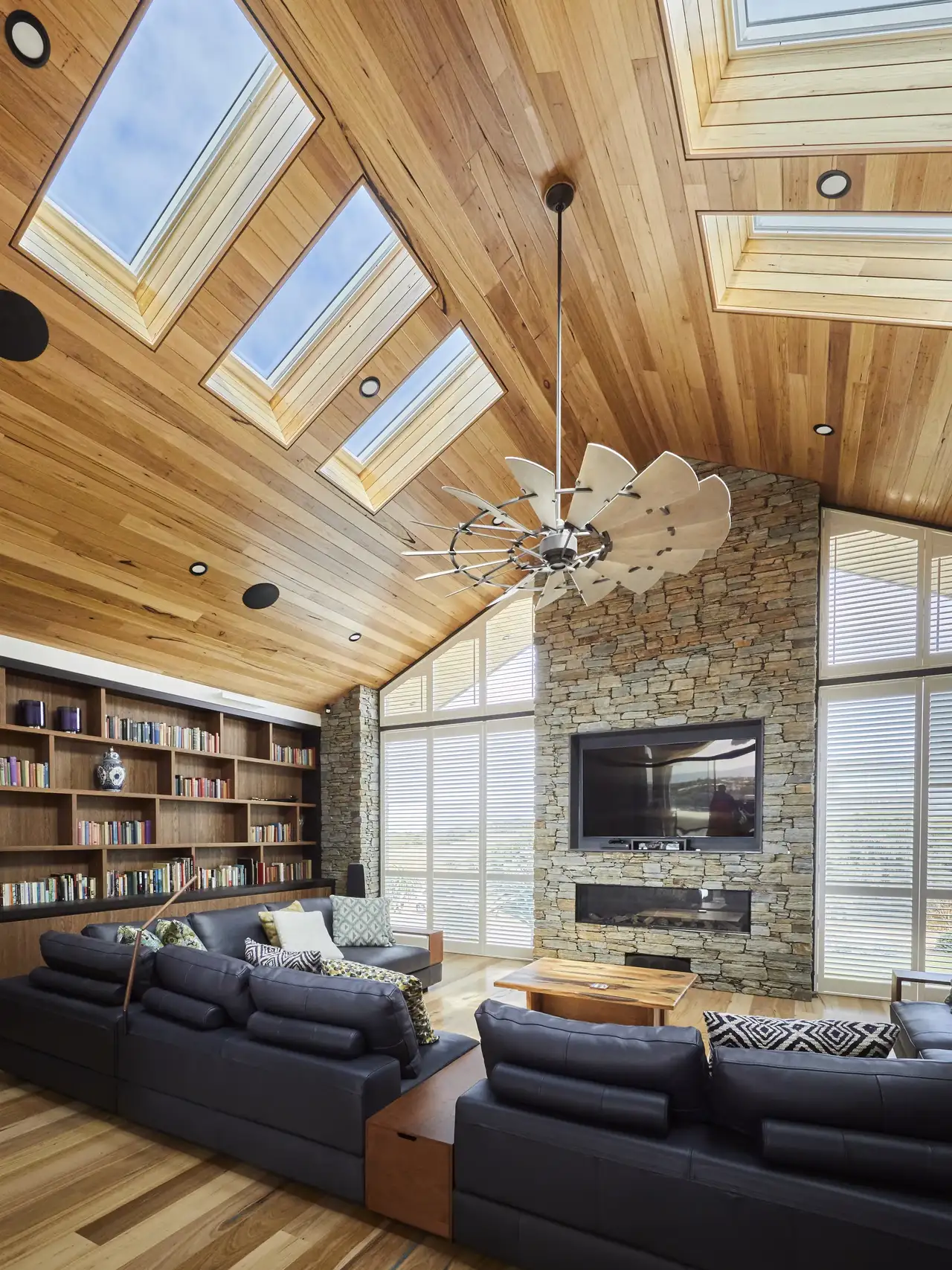 Soggiorno in stile rustico contemporaneo con soffitto in legno, pareti in pietra e finestre per tetti che illuminano l’ambiente.