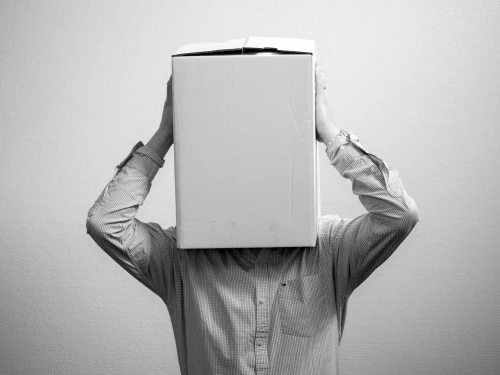 Person indoors holding a cardboard box over their head, face hidden.