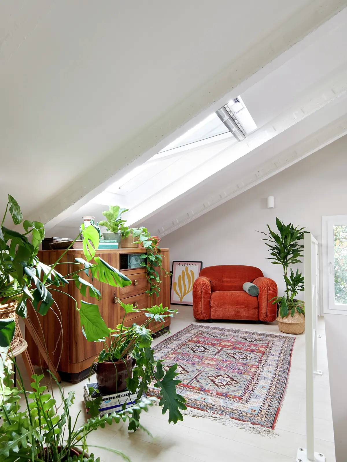 Chambre de comble lumineuse avec fenêtre VELUX, plantes, meubles vintage et canapé orange.