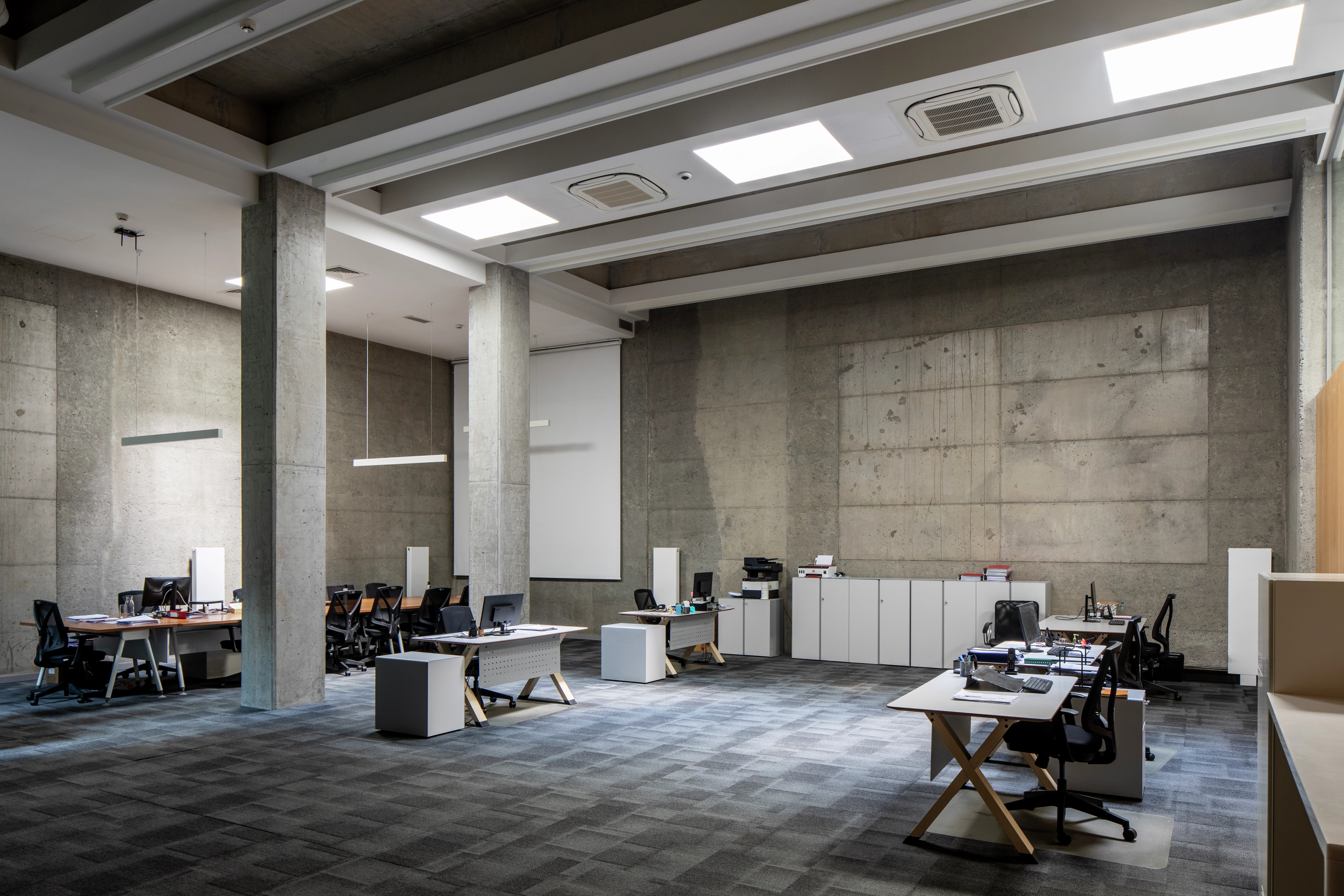 Spacious office with concrete walls, desks, chairs, and modern lighting.