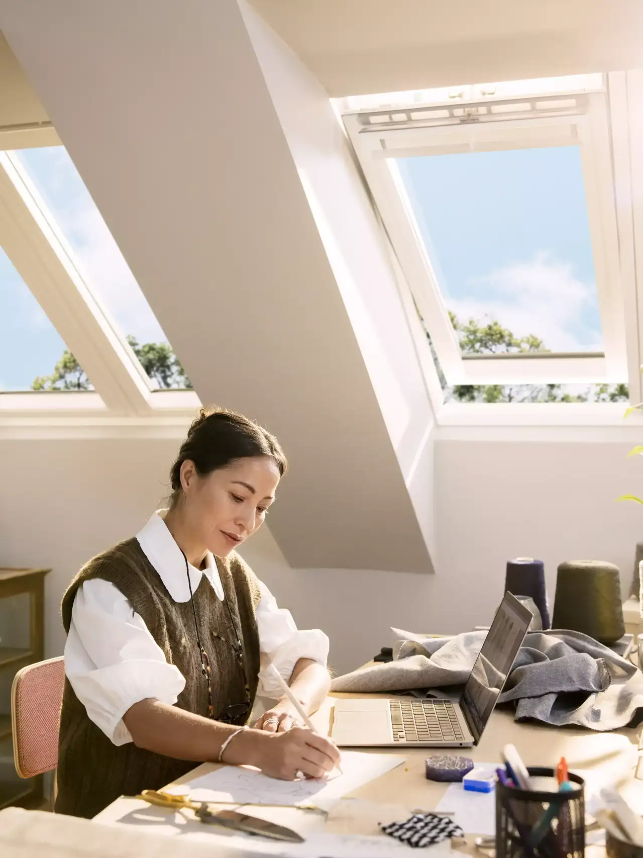 Homeoffice mit VELUX Dachflächenfenster, das reichlich Sonnenlicht über einen aufgeräumten Arbeitsplatz mit Laptop und Utensilien liefert.