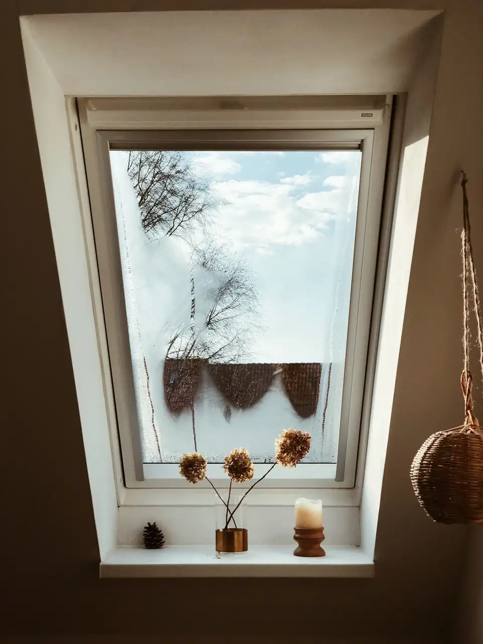 Grenier avec fenêtre de toit VELUX, fleurs séchées et bougie sur le rebord.