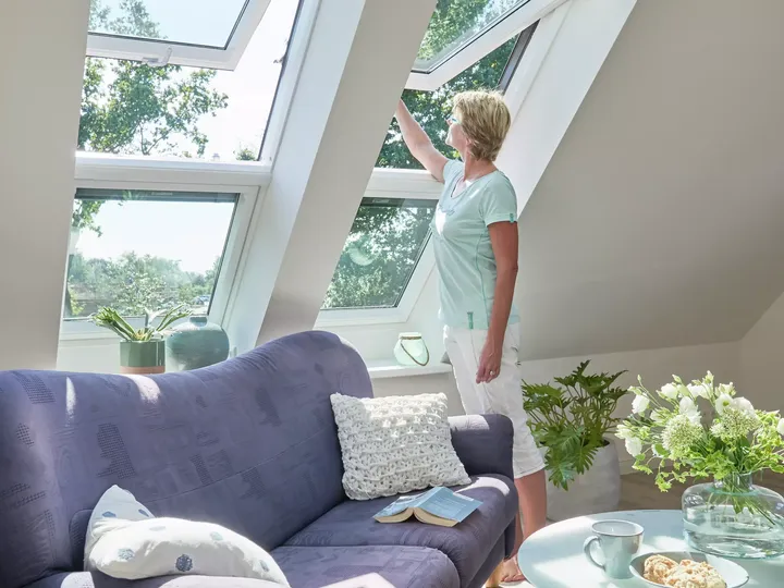 Frau im Dachboden-Wohnzimmer mit VELUX-Fenster, blauem Sofa und frischen Blumen.