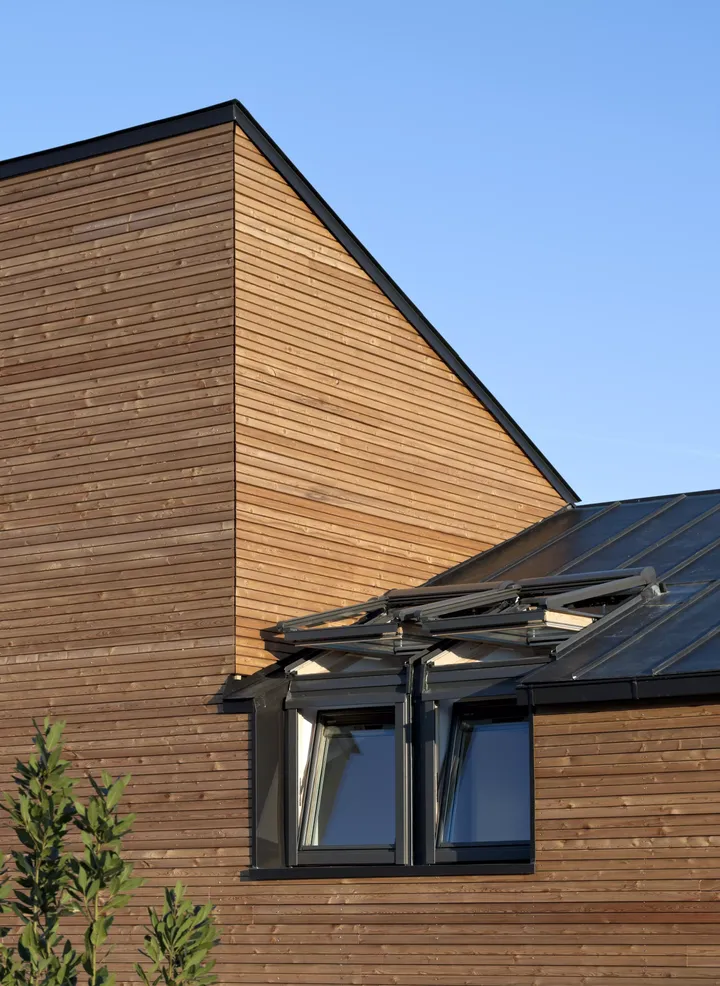 Maison Air et Lumière’nin dış cephesi; eğimli çatısında çok sayıda VELUX çatı penceresi bulunan, ahşap kaplamalı bir ev. Doğal havalandırma ve ışık için en iyi şekilde tasarlanmış | VELUX