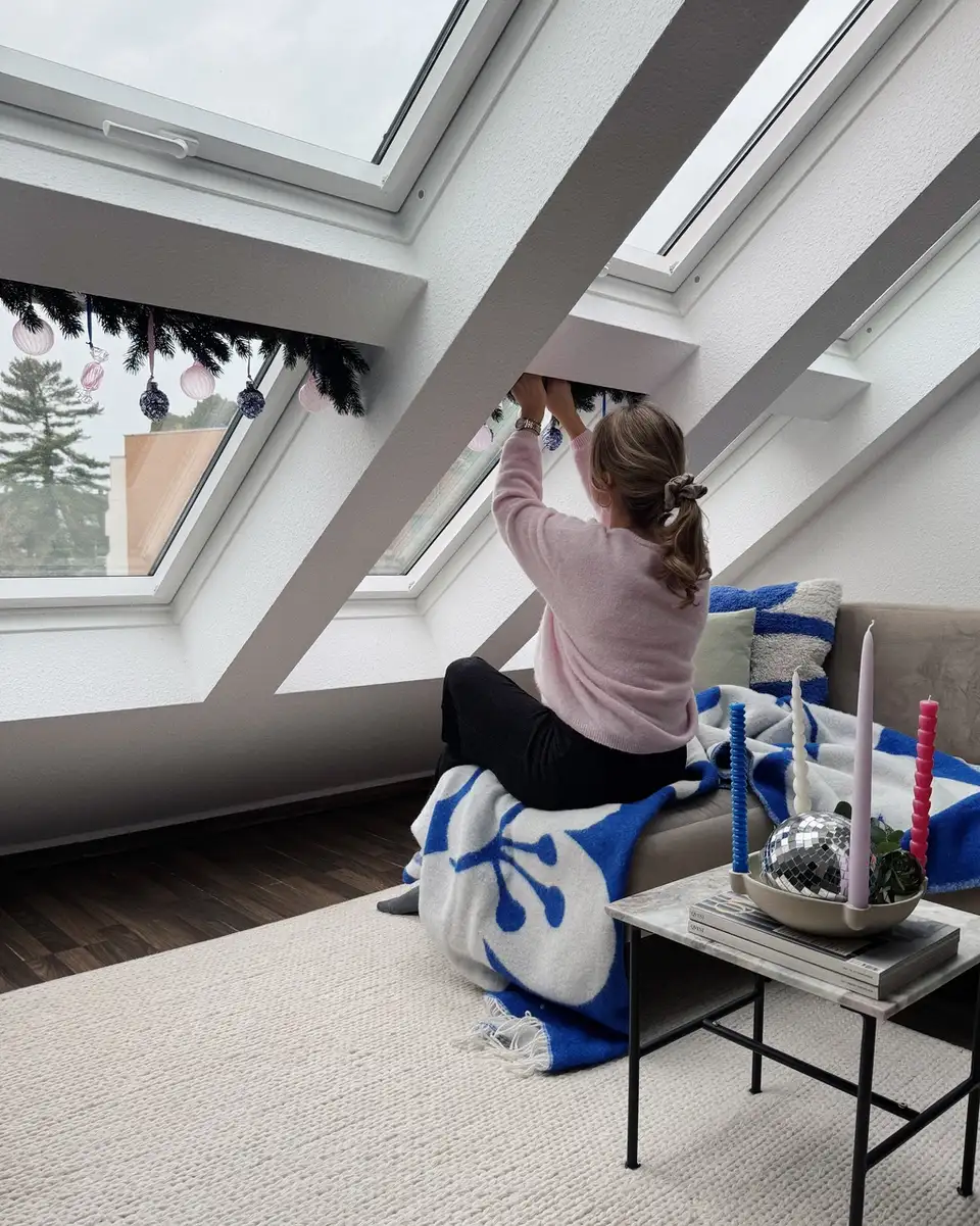 Une femme décore les fenêtres de toit avec les décos de Noël déco fenêtre noël – VELUX