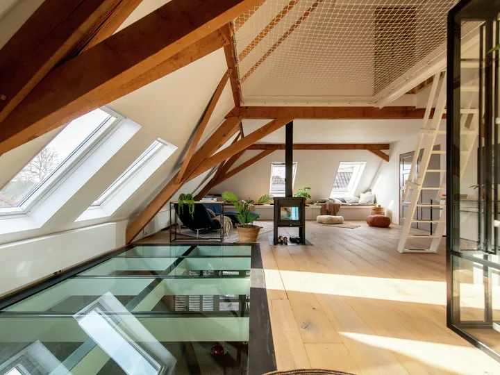 Heller Dachboden-Wohnraum mit VELUX-Fenstern, hölzernen Balken und Glas-Bodenpaneelen.