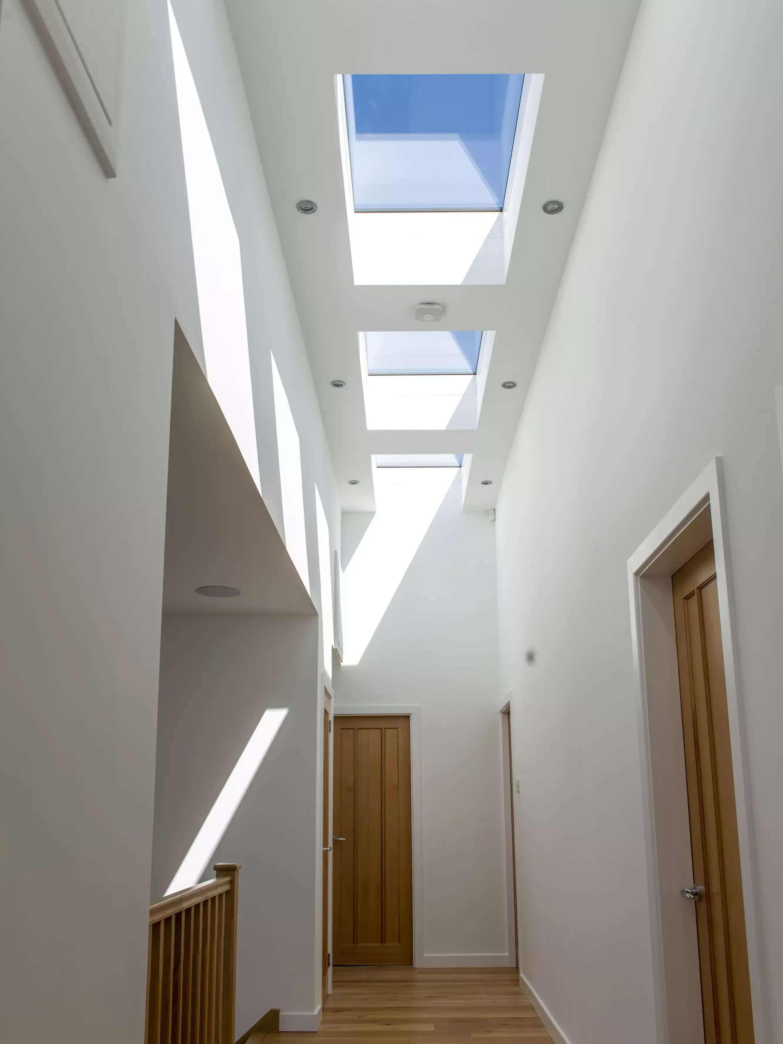 Modern corridor with natural lighting from VELUX roof windows, wooden floors, and minimalist design.