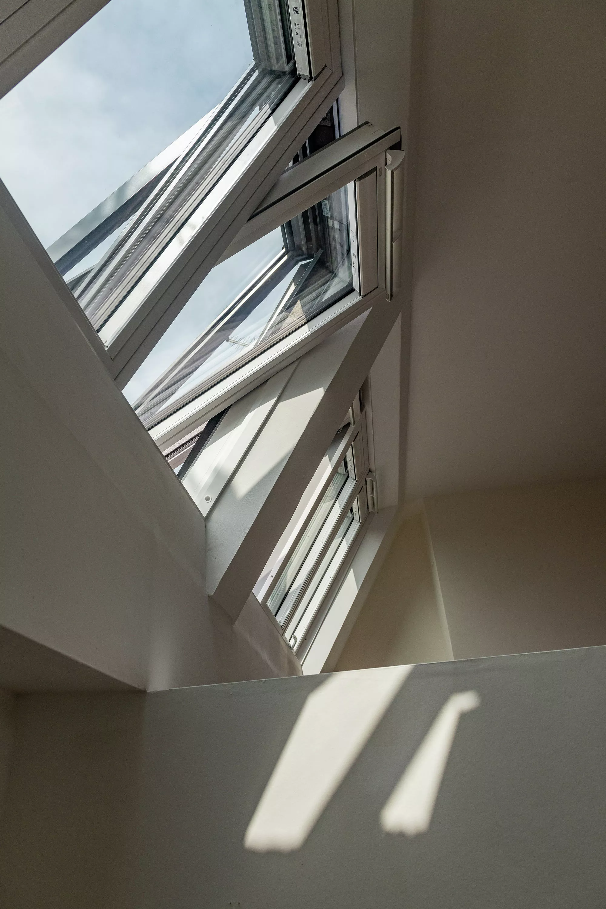 Ouvrez la fenêtre de toit VELUX éclairant un escalier avec la lumière naturelle, créant des ombres dynamiques.