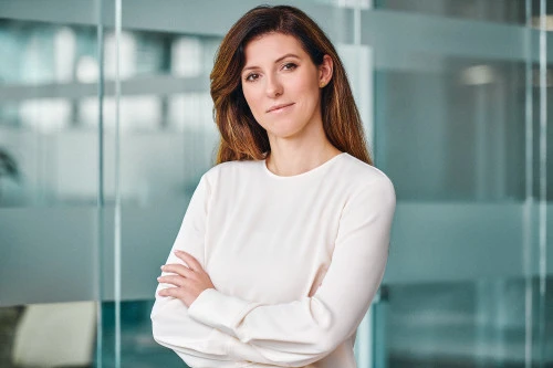 Woman in white top standing with folded arms in a modern glass office corridor