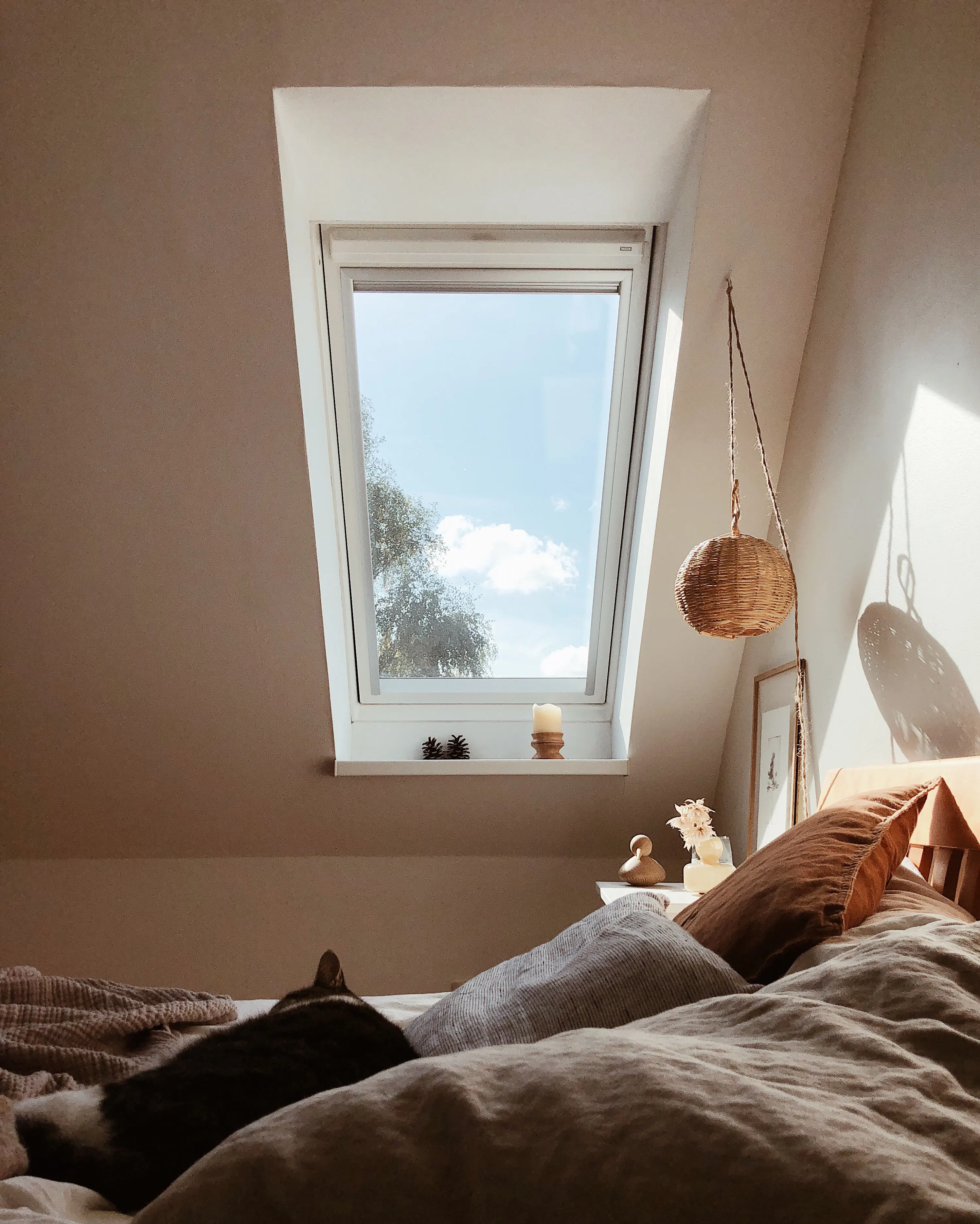 Attic bedroom with sloped ceiling and VELUX roof window, cozy bedding.