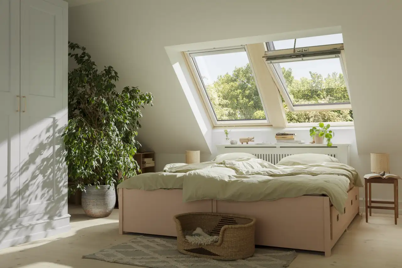 Großes Bett mit Schubläden umgeben von Pflanzen und einem Nachtisch steht unter zwei Dachfenstern | VELUX Magazin
