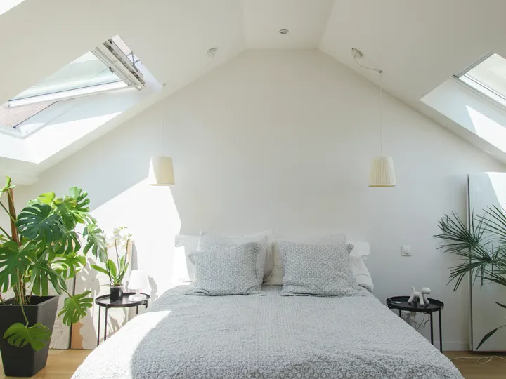 Gemütliches Dachboden-Schlafzimmer mit VELUX Dachflächenfenstern und grünen Pflanzen.