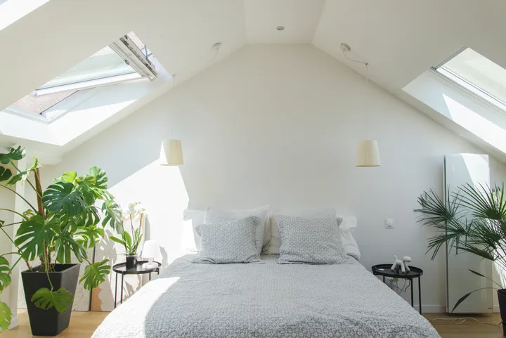 Schlafzimmer im Dachboden mit VELUX Dachflächenfenster, grauer Bettwäsche und grünen Pflanzen.
