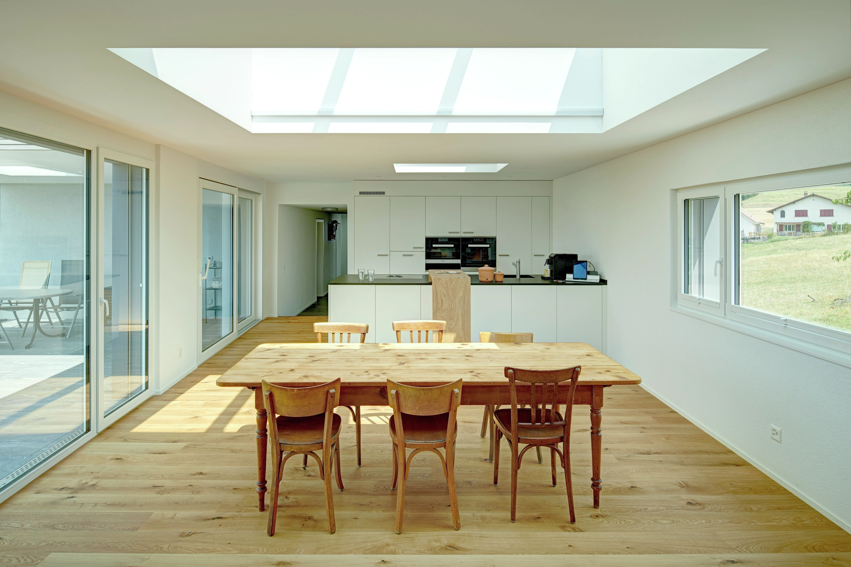 Svetlá kuchyňa s dreveným stolom, strešným oknom VELUX a modernými spotrebičmi.