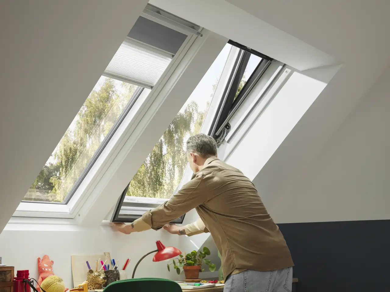 Un uomo apre e controlla una delle due finestre per tetti VELUX installate nel suo ufficio in casa.