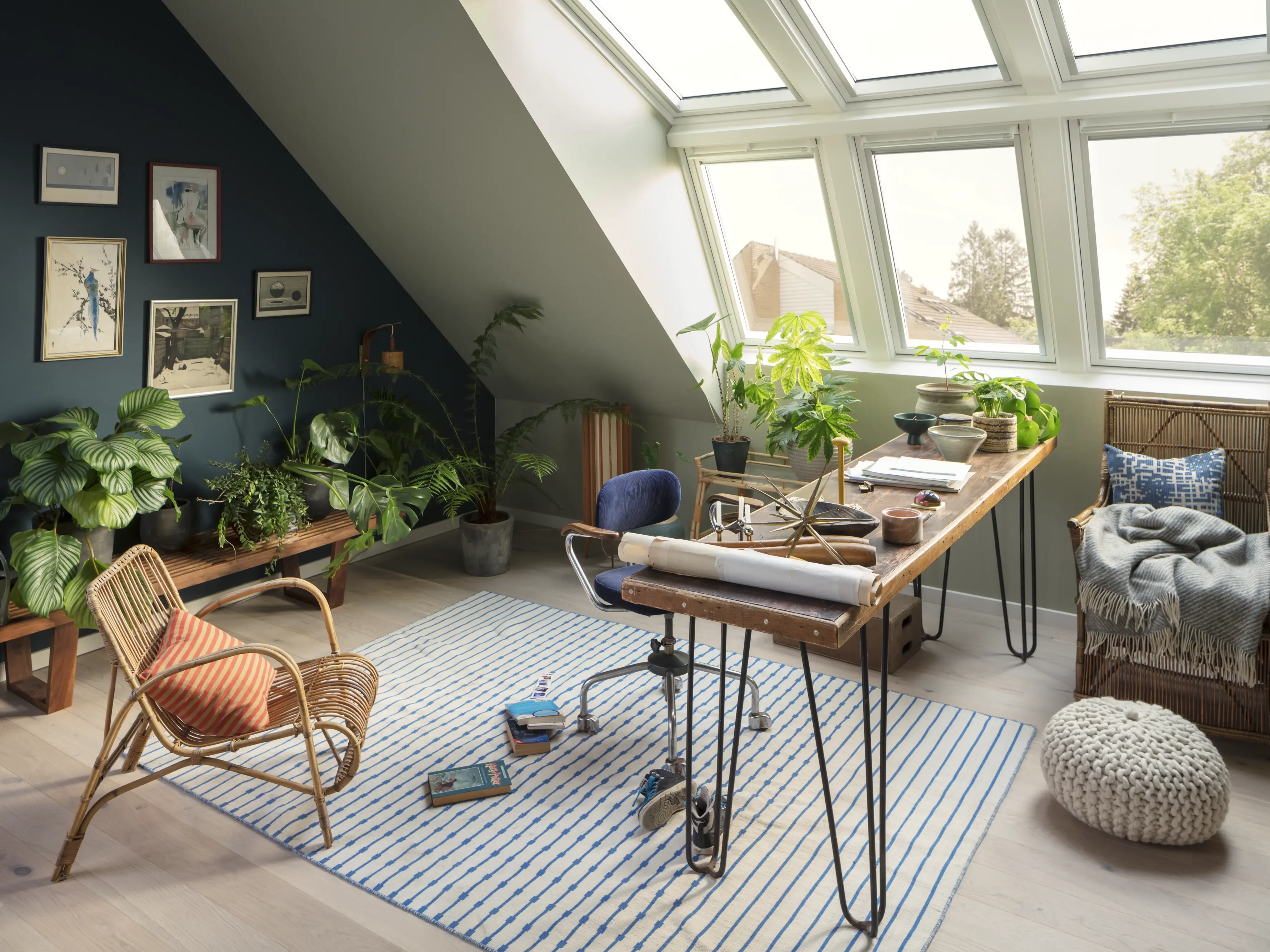 Attic workspace with sloped ceiling and VELUX roof windows, filled with plants.