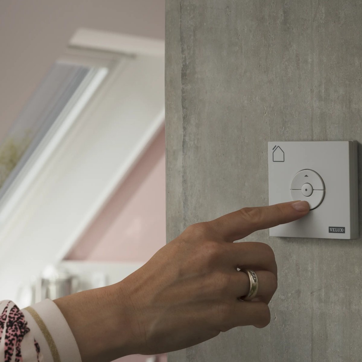 Hand using smart control panel for VELUX roof window in attic room.