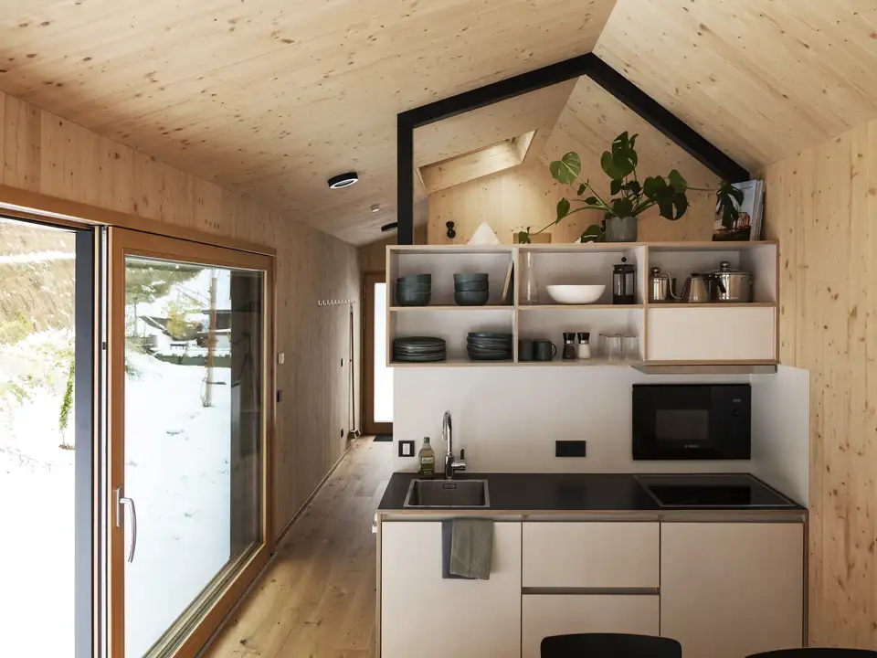 Cucina moderna con pareti in legno, soffitto a falda e ampia finestra verticale con vista.