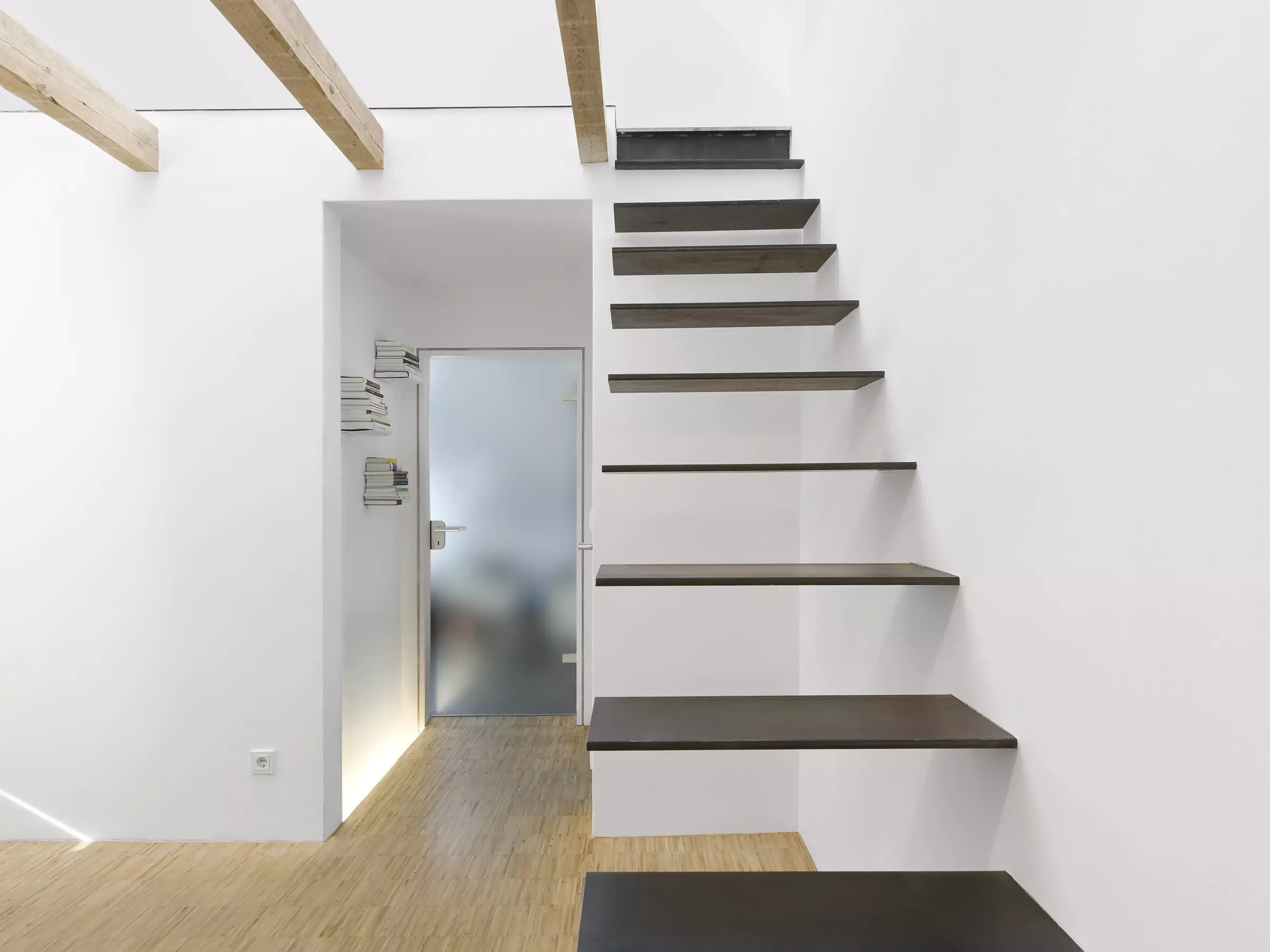 Interno minimalista con moderna scala sospesa in legno e pareti bianche.