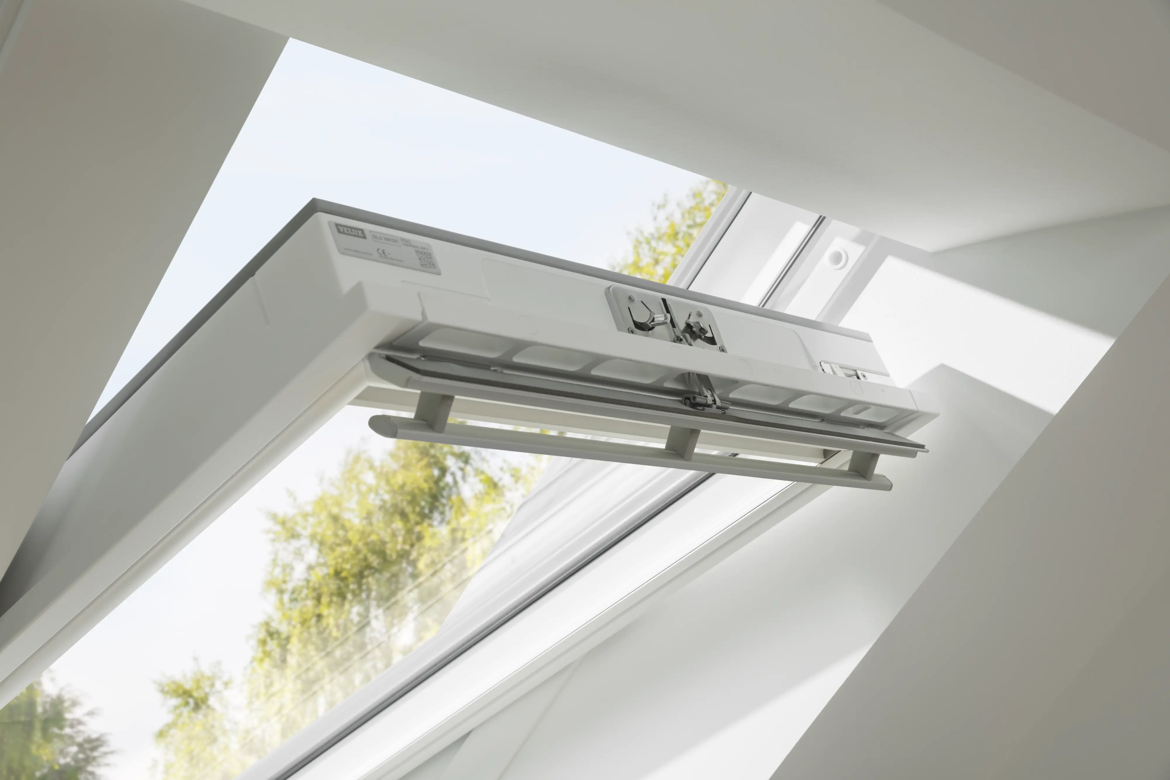 Nyitott VELUX tetőablak fehér belső felülettel egy világos tetőtéri helyiségben, a műanyag felületű vagy karbantartásbarát ablakok egyszerű tisztításának szemléltetésére. 