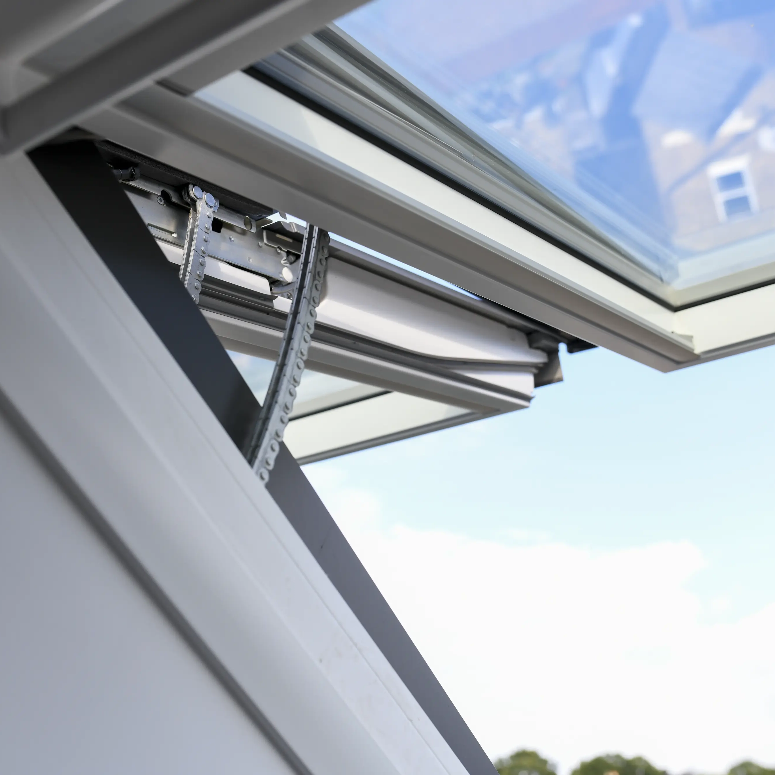 Open VELUX roof window on sloped ceiling, view of rooftops and sky.