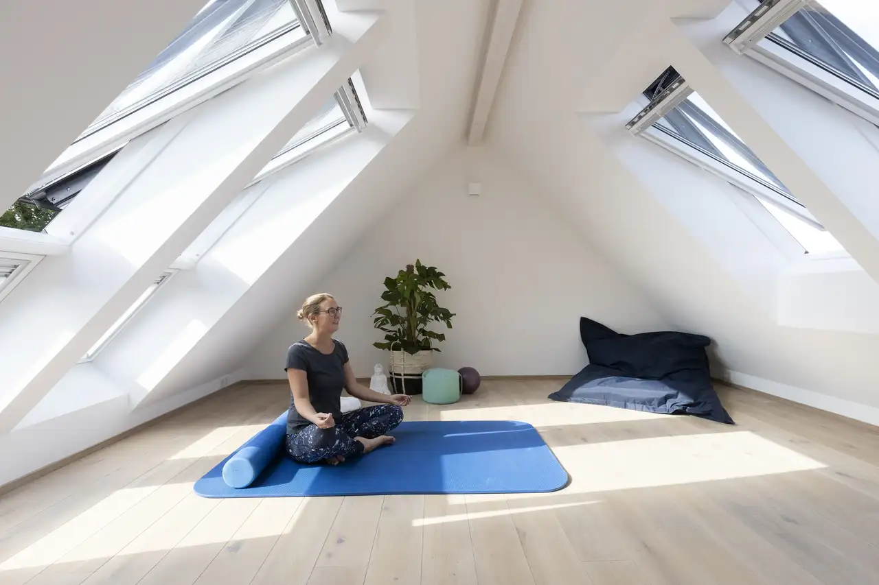 Femme en méditation assise en tailleur dans une pièce mansardée avec fenêtres de toit VELUX de chaque côté