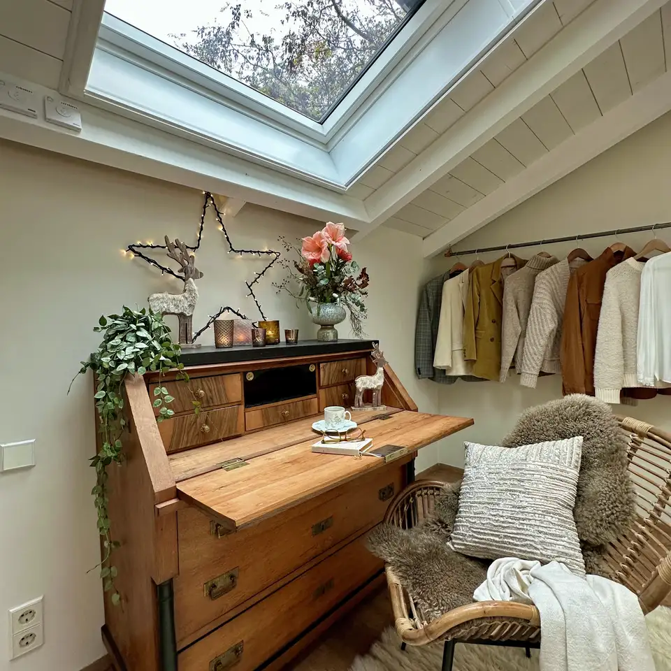 Secrétaire en bois sous une fenêtre de toit, décoré de fleurs et de guirlandes lumineuses dans une chambre mansardée rustique. 