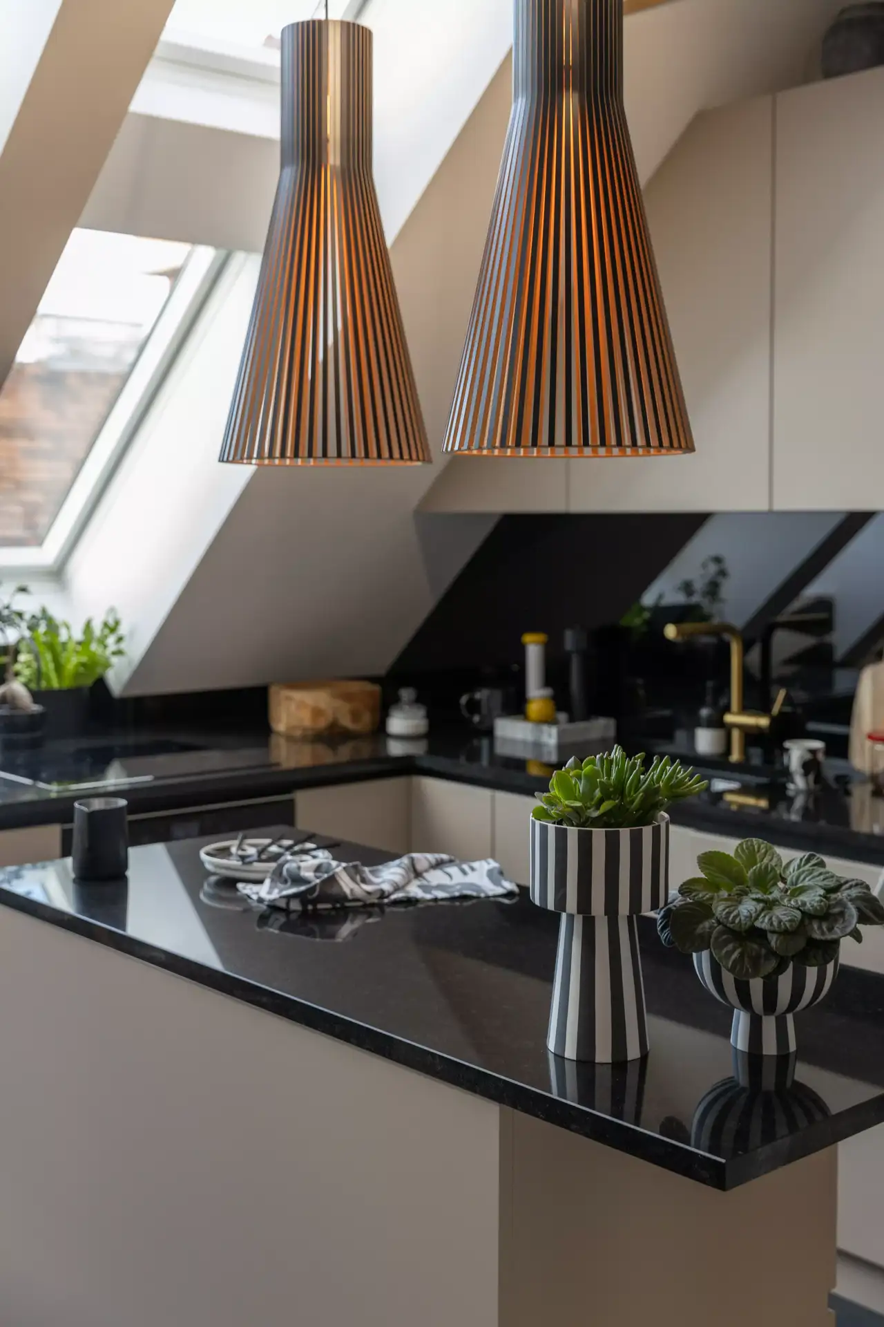 Moderne Küche mit schwarzer Arbeitsplatte, Hängeleuchten und VELUX Dachflächenfenster.