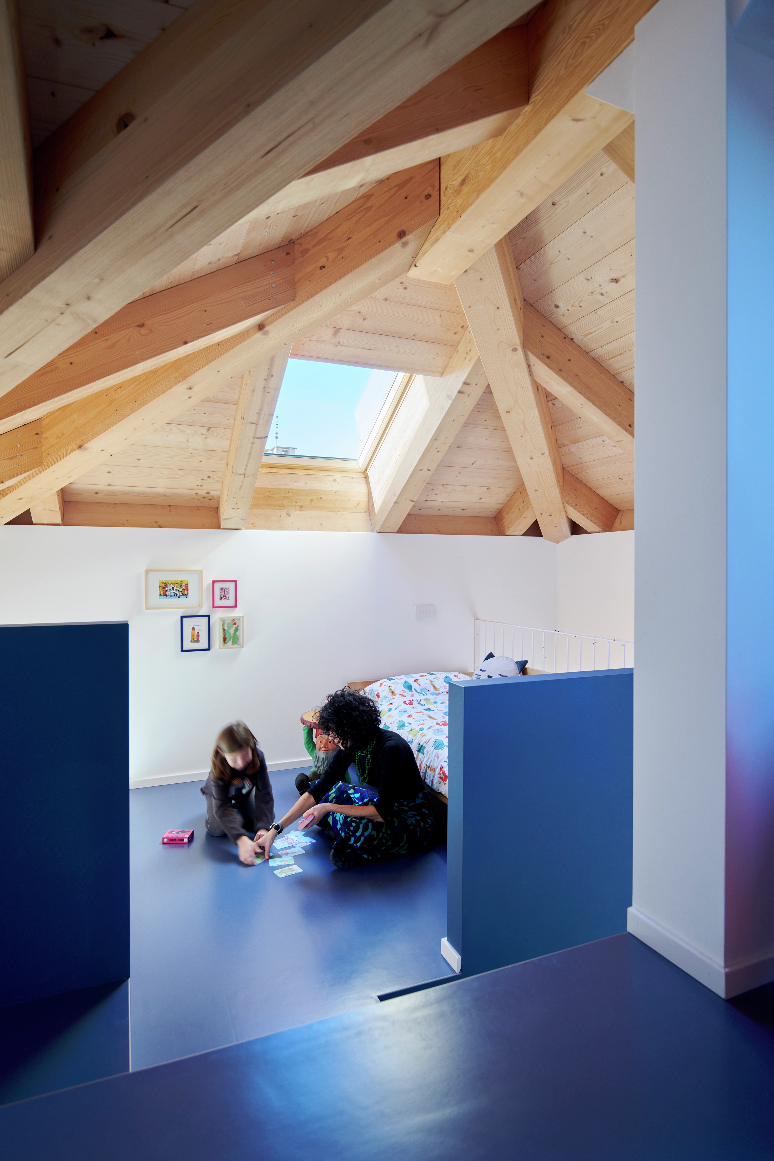 Salle de jeux dans le comble avec des poutres en bois et une fenêtre de toit VELUX, lit et espace de jeu.