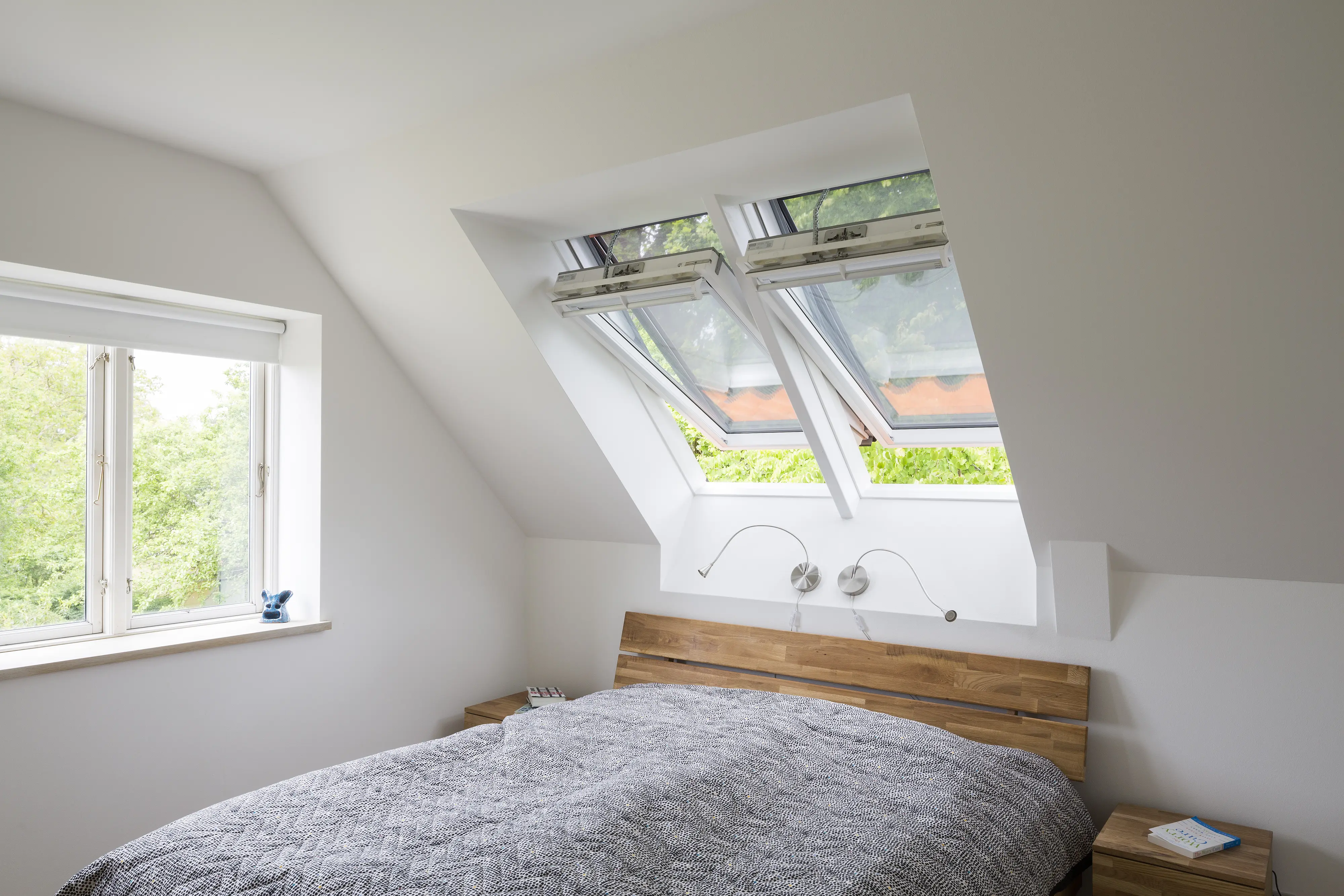 Dormitor la mansardă cu tavan înclinat și ferestre de mansardă VELUX deschise.