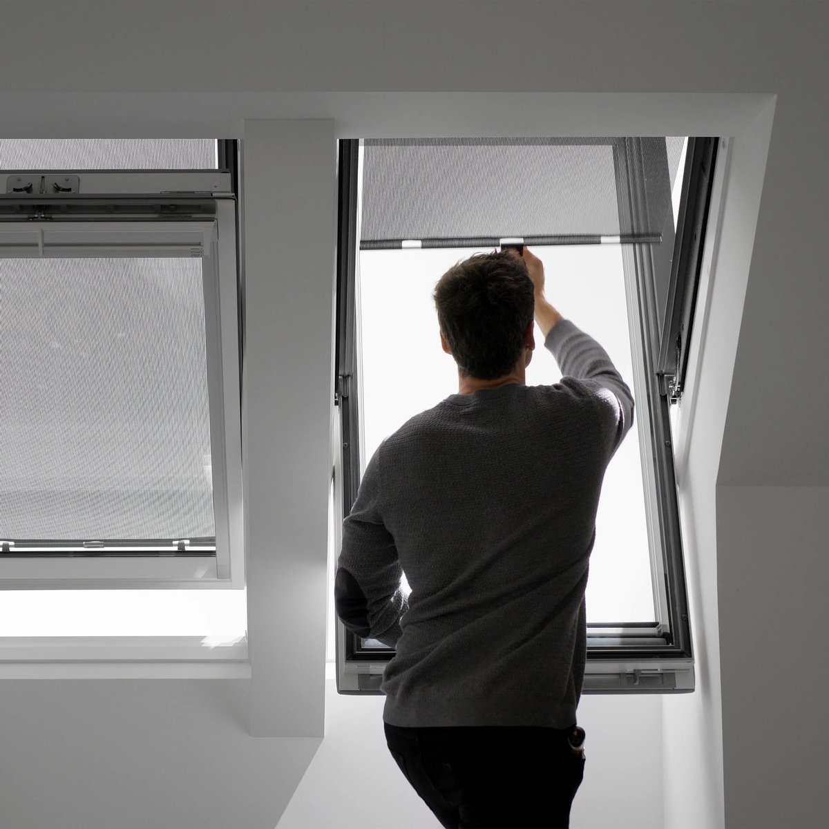 Man adjusting VELUX roof window in a bright attic room.