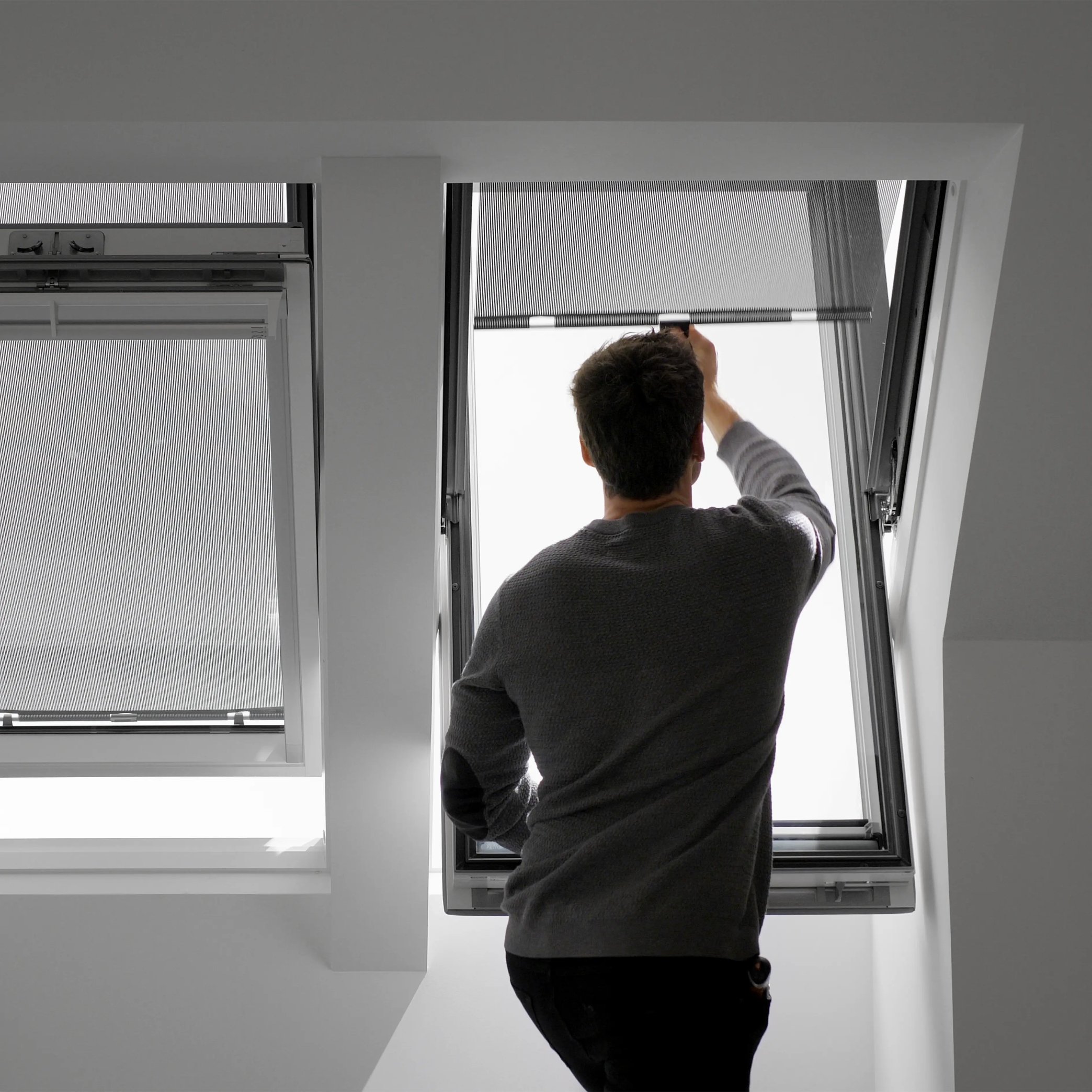 Man adjusting VELUX roof window in a bright attic room.
