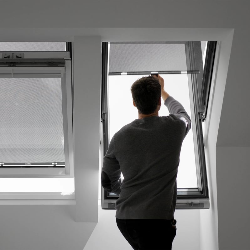 Man adjusting VELUX roof window in a bright attic room.